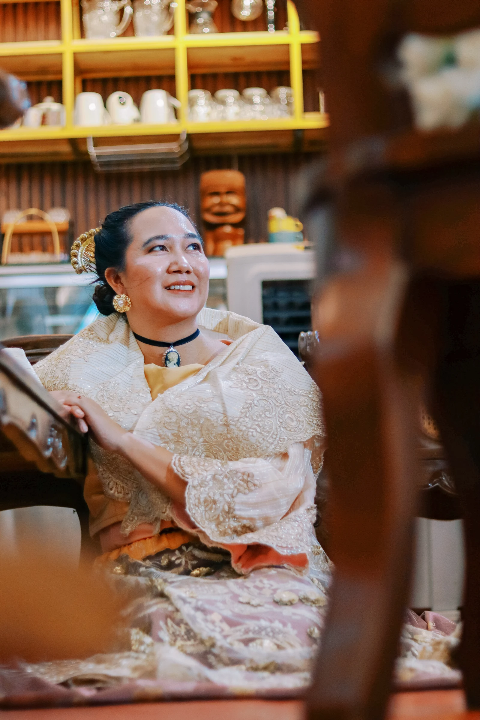 Rubie looking up at Clive across a cafe table in her embroidered Filipiniana