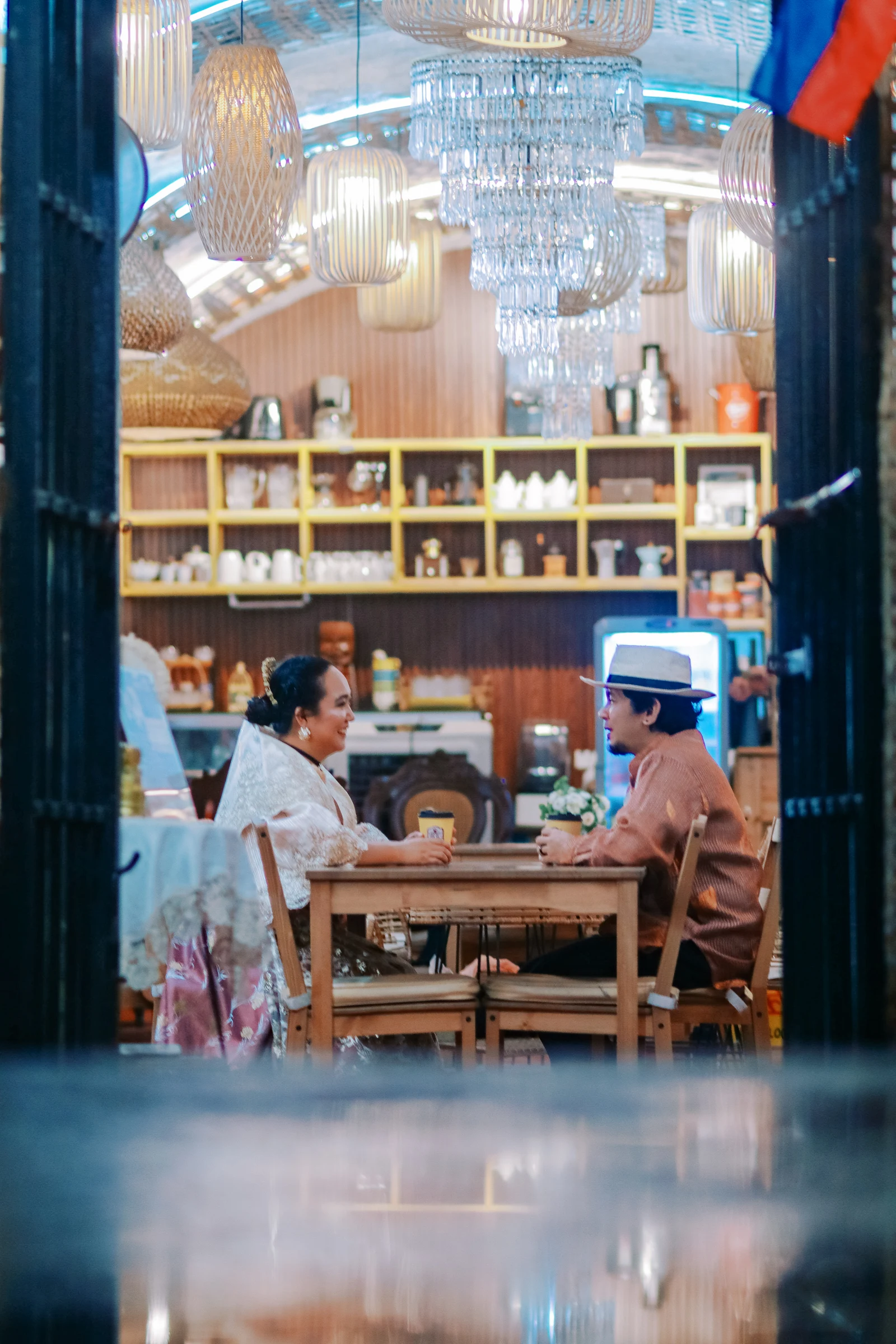 Clive and Rubie sharing coffee beneath woven lamps and a chandelier