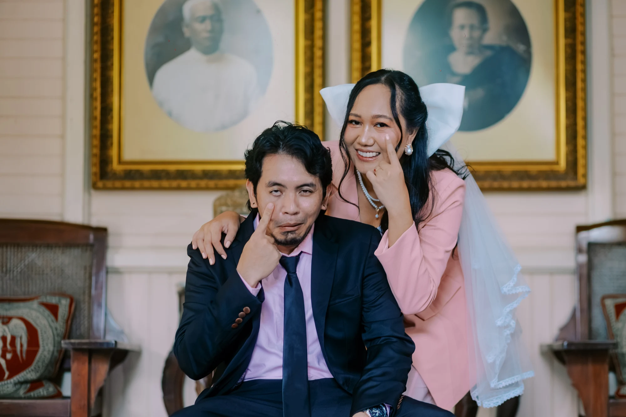 Clive and Rubie making playful faces beneath antique portraits