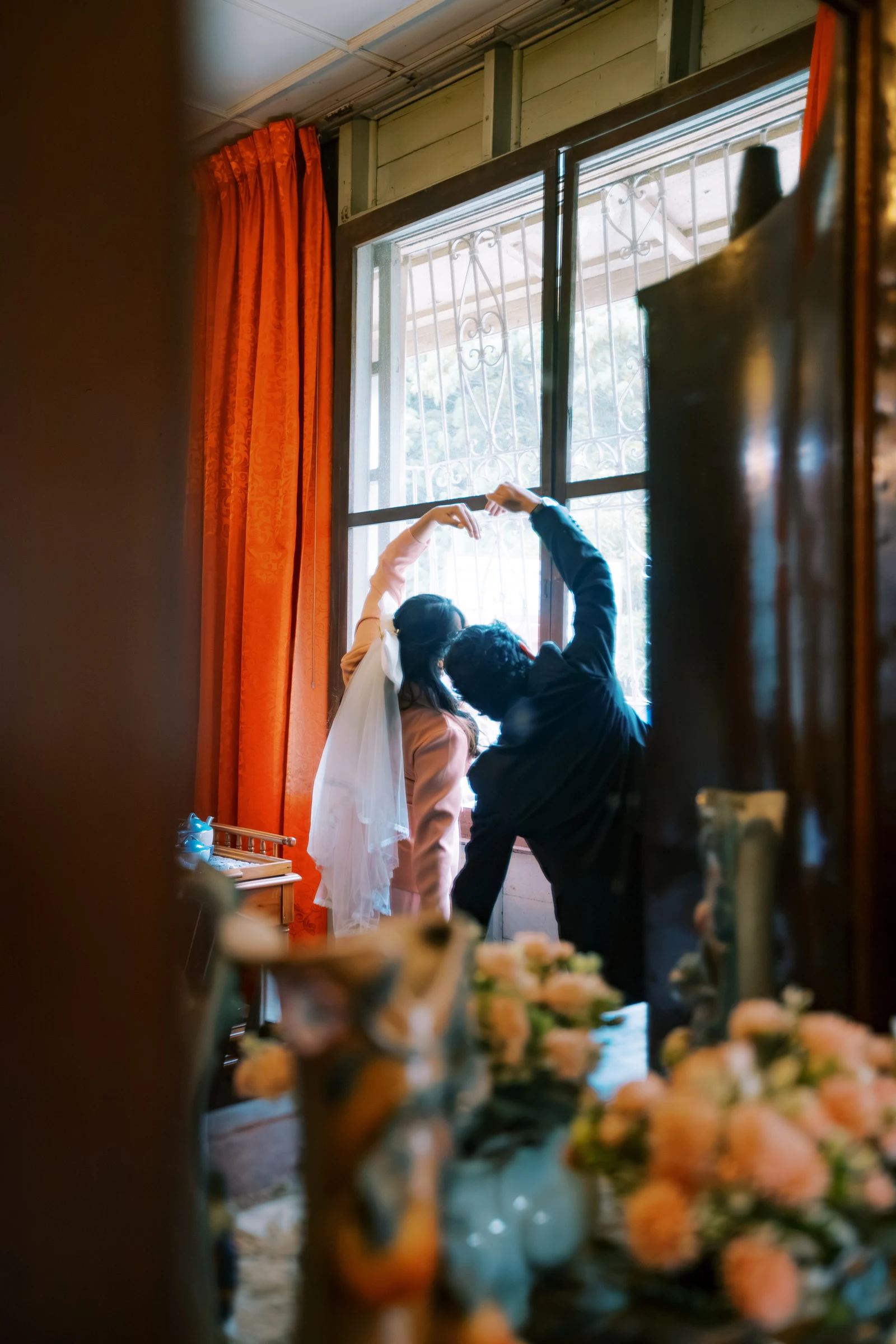 Clive and Rubie making a heart with their arms beside a sunlit heritage window